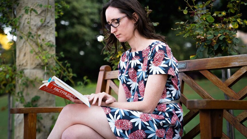 Dr Natasha Moore reads a book on a park bench.