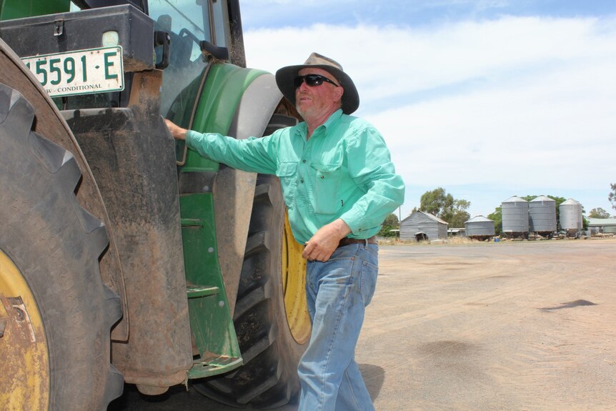 A man in sunglasses gets ready to board a tractor. 