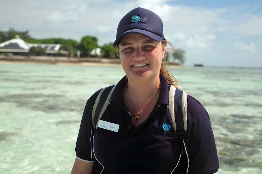 Cate Streng stands on a beach with a clear reef in the background