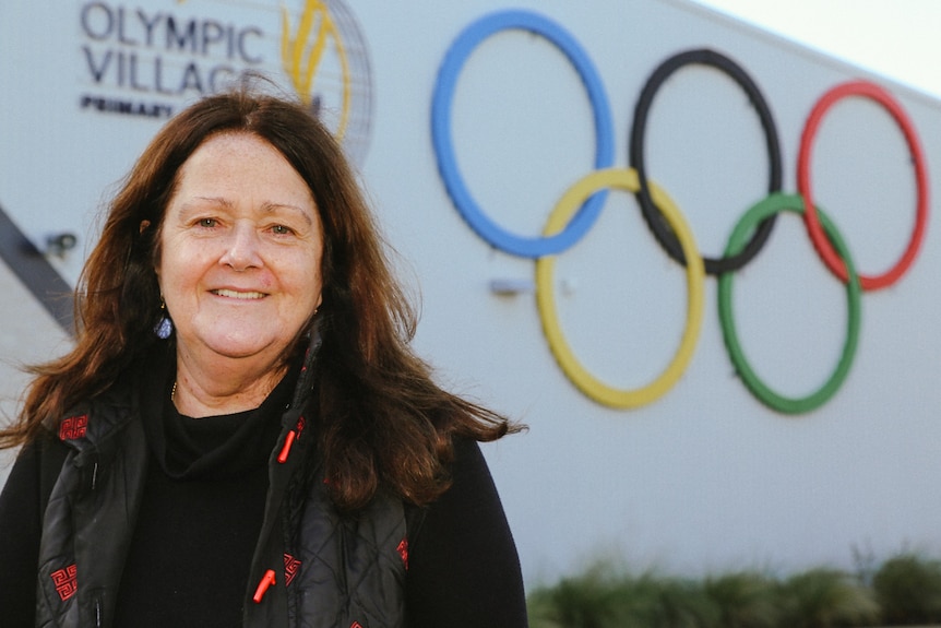 A woman stands in front of a wall with the Olympic rings displayed.