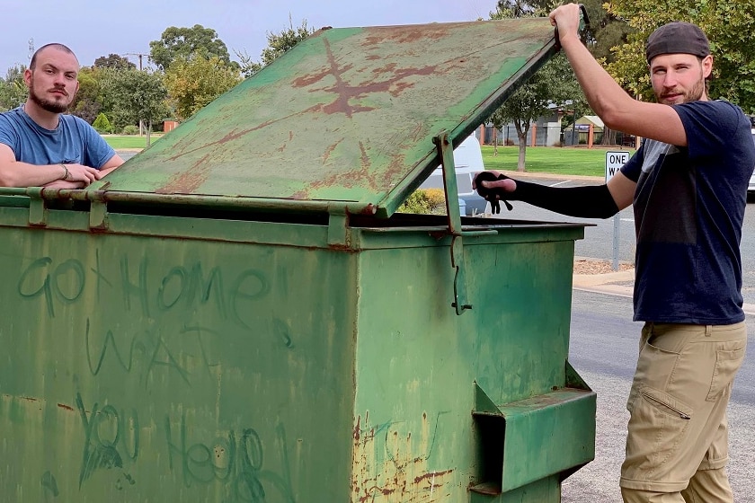 backpackers standing near a bin with the writing Go home at their hostel.