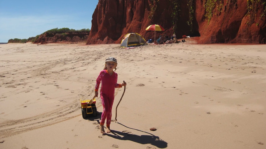 A girl walks on a beach with red cliffs