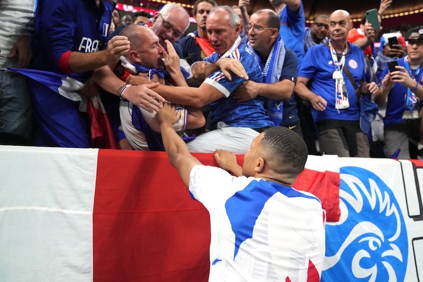 Kylian Mbappe holds his hand up to a fan