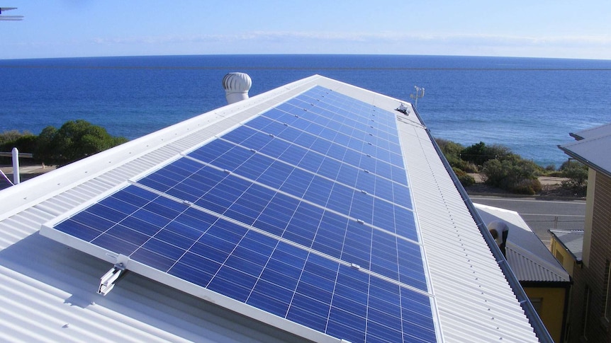 Solar panels on the white roof of a house by the ocean.
