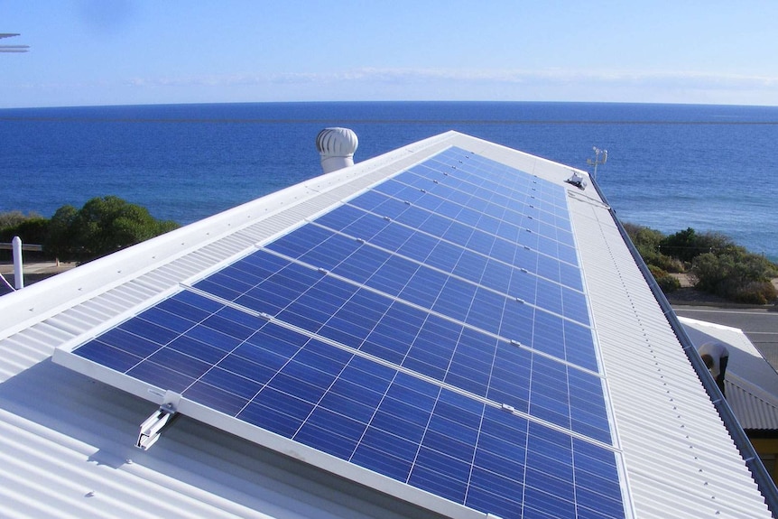 Solar panels on the white roof of a house by the ocean.