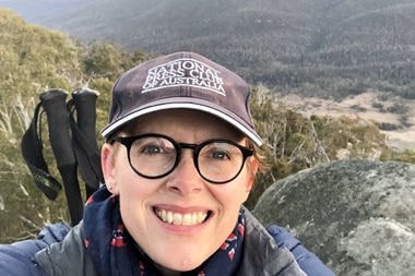 Woman taking selfie with mountains and bush in background.