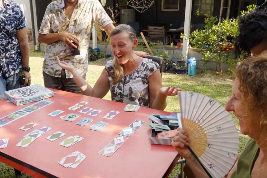A group of people play a card game in a backyard.
