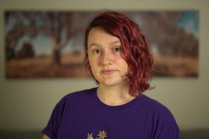 A young woman in her 20s with short red hair looking at a photographer.