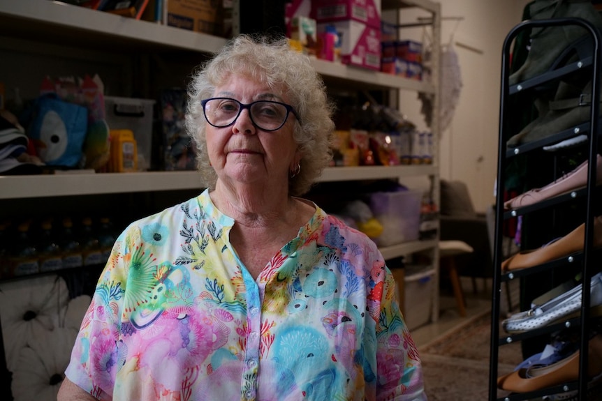 A woman with short blonde hair, glasses in a colourful shirt in an op shop