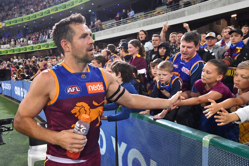 A male AFL player holds a bottle of sports drink as he shakes hands with a spectator in the crowd after a match.