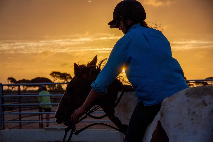 Lauren Hughes rides a newly trained horse as the sun sets.