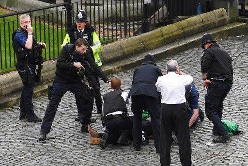 Police in London surround a man on the ground and aim a gun at him.
