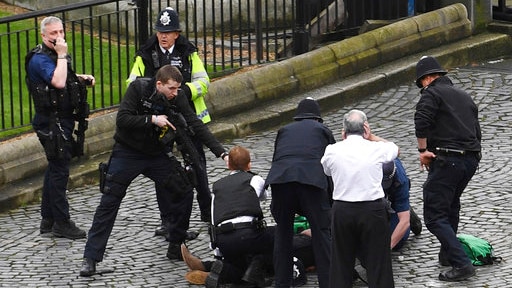 Police in London surround a man on the ground and aim a gun at him.