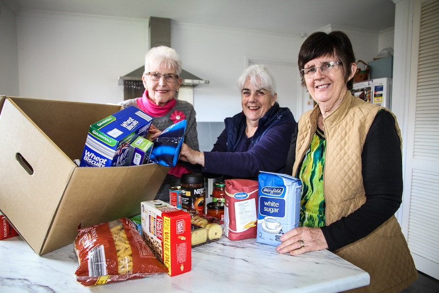 Three CWA members in the kitchen with a box of goods ready to be delivered to farmers.