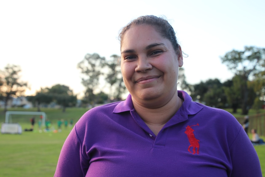 Kiara se tient devant un terrain de football avec des enfants jouant en arrière-plan.