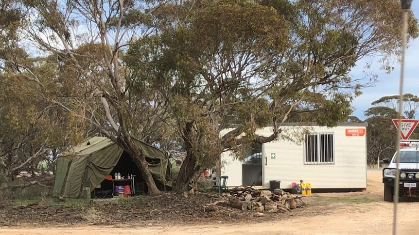A tent, transportable building and a police car at a scrubland border crossing.