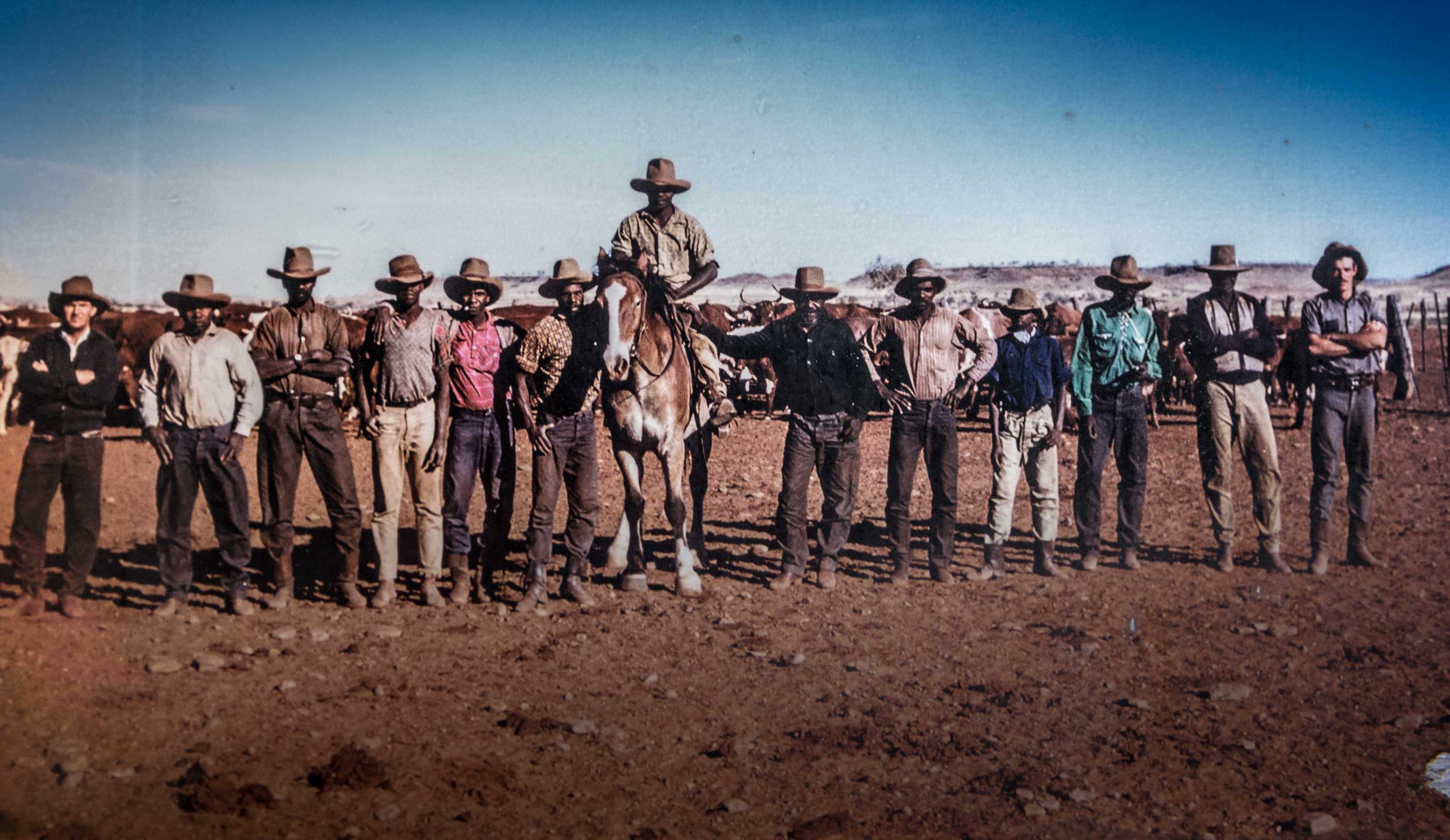 A group of stockmen stand in a line with one mounted on a horse.