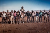 A group of stockmen stand in a line with one mounted on a horse.