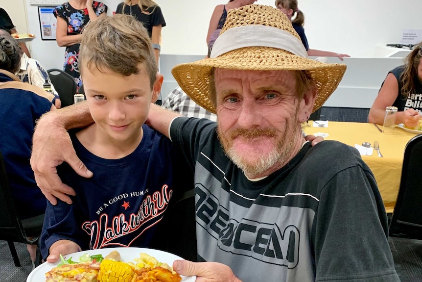 8-year-old Taz Traill serves food to a man wearing a hat at a Gold Coast soup kitchen.