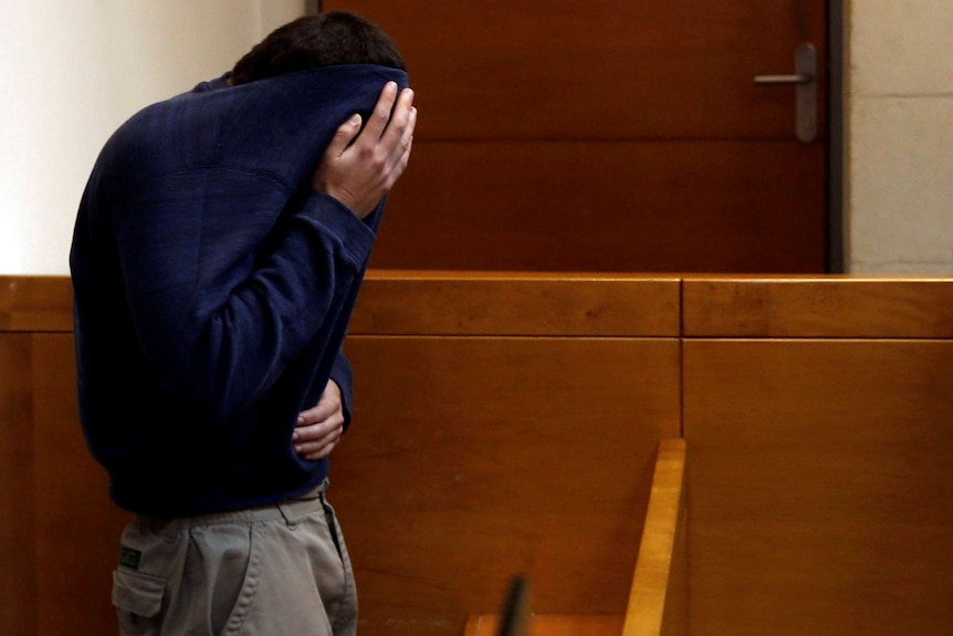 A teen in an Israeli court, covering his face with his jumper