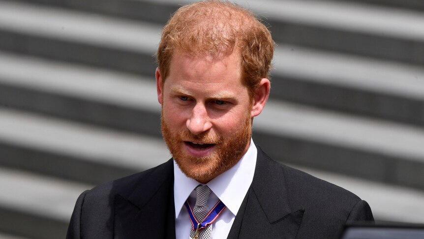 Prince Harry walks down stairs wearing a suit and tie.