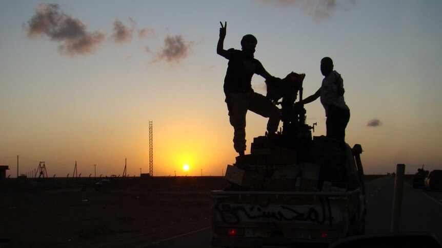 Libyan fighters stand on top of a combat vehicle as the sun sets behind them.