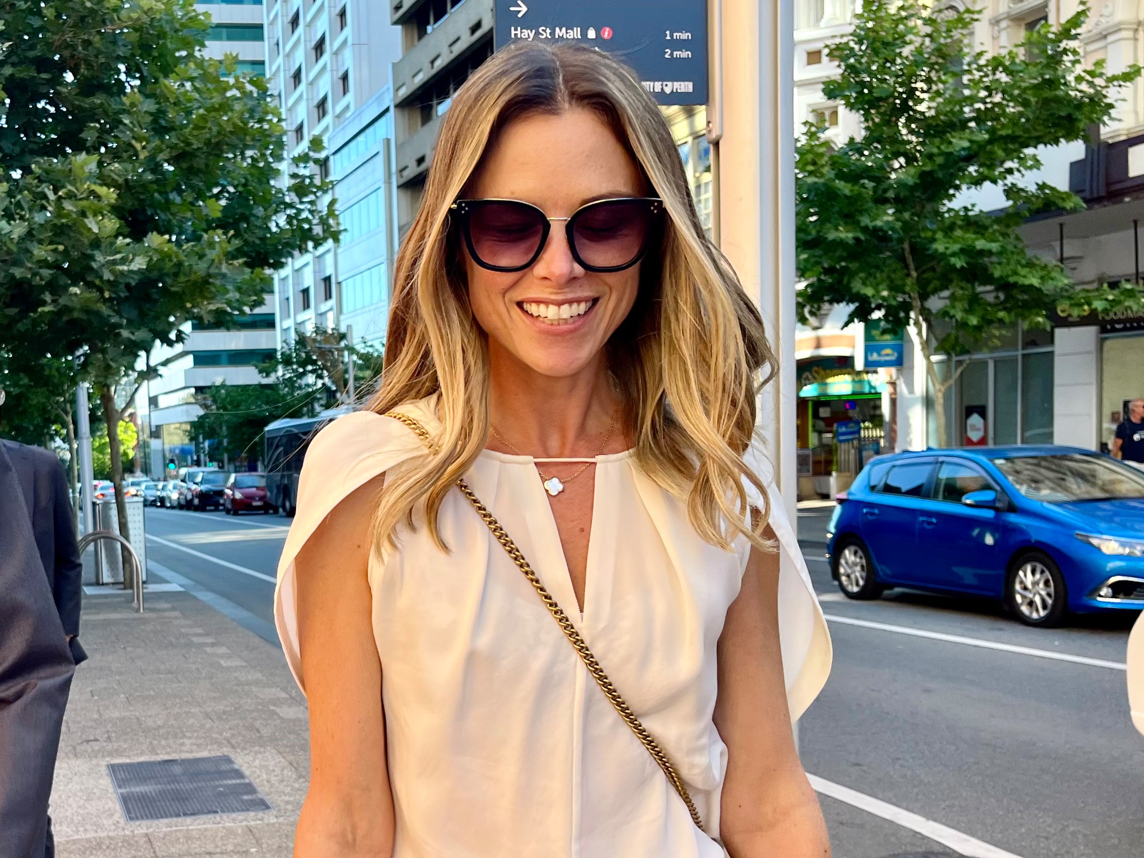 Headshot of a woman in sunglasses walking in a city street