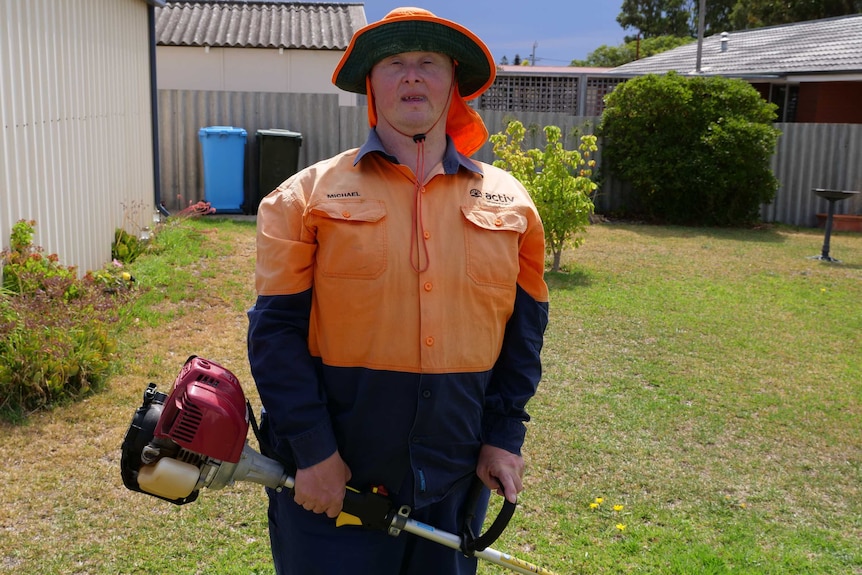 A man stands wearing an orange uniform holding a string trimmer, also known as a whipper snipper.