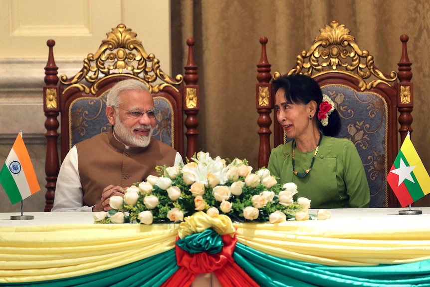 Narendra Modi and Aung San Suu Kyi sit beside each other and talk.