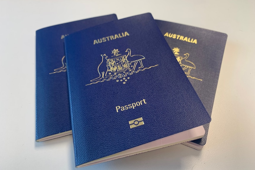 Three Australian passports in a little pile. They have the gold coat of arms on them and are mostly blue.
