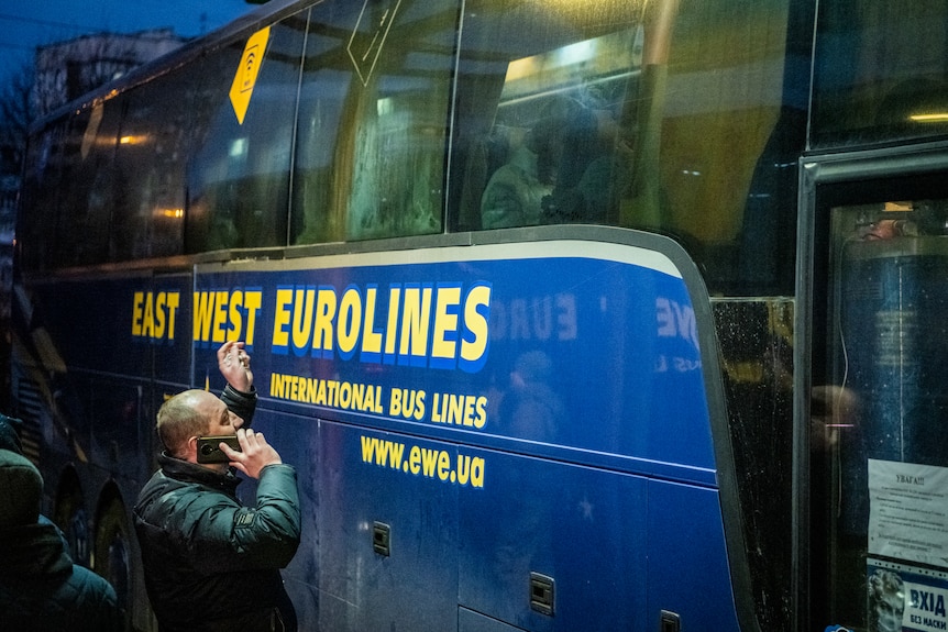 A man stands outside a bus with EAST WEST EUROLINES painted on the side. He talks into a phone and waves