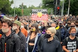 A large crowd wearing face masks marching in Melbourne, wearing t-shirts or holding signs in support of Aboriginal Australians.