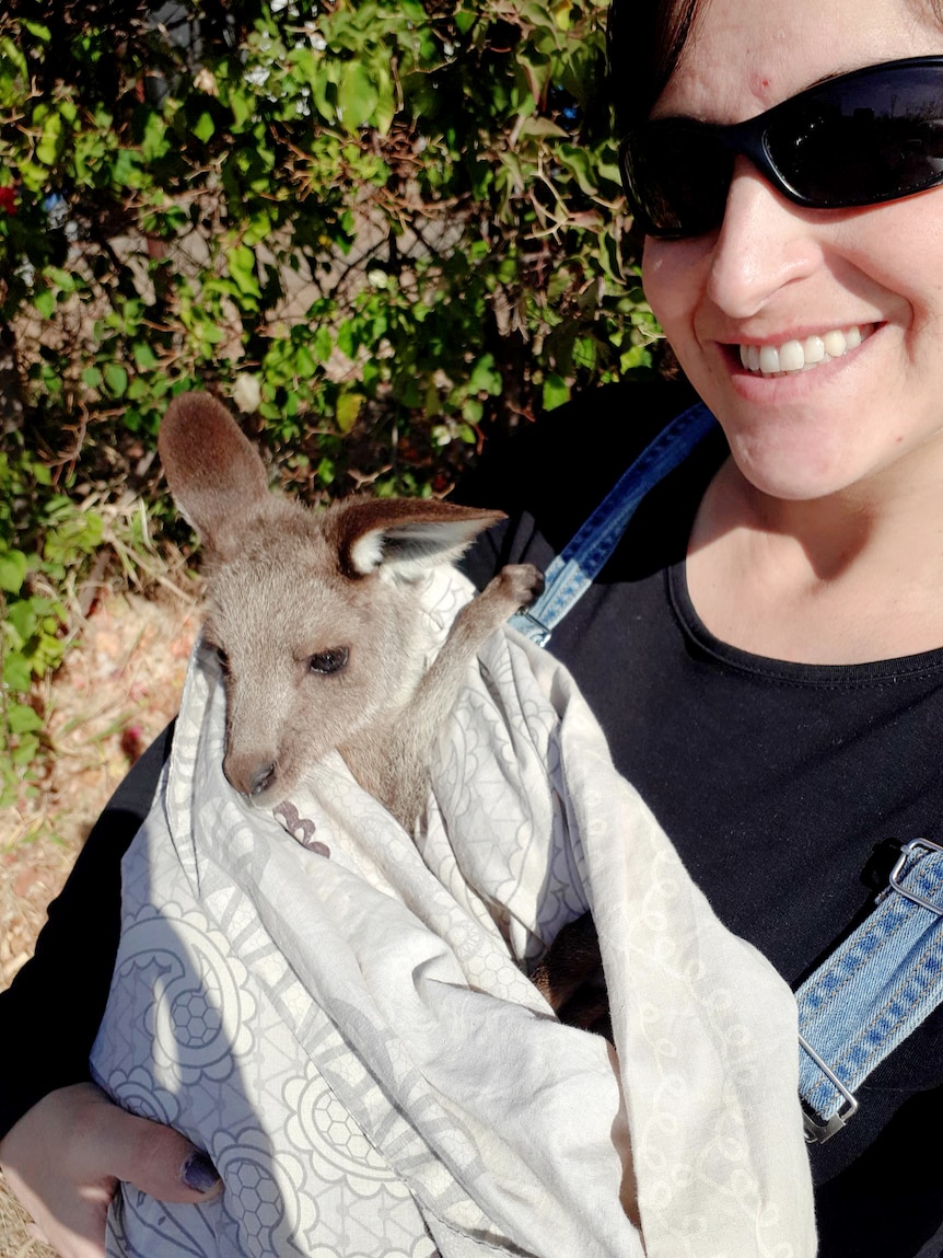 Woman stands holding a wallaby, she is smiling