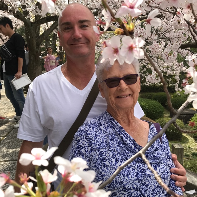 Younger man and older woman stand among the cherry blossoms