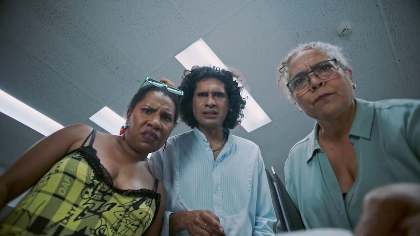 Low angle shot of three people, woman in yellow top, man blue shirt, and woman wearing glasses, staring down puzzled expressions