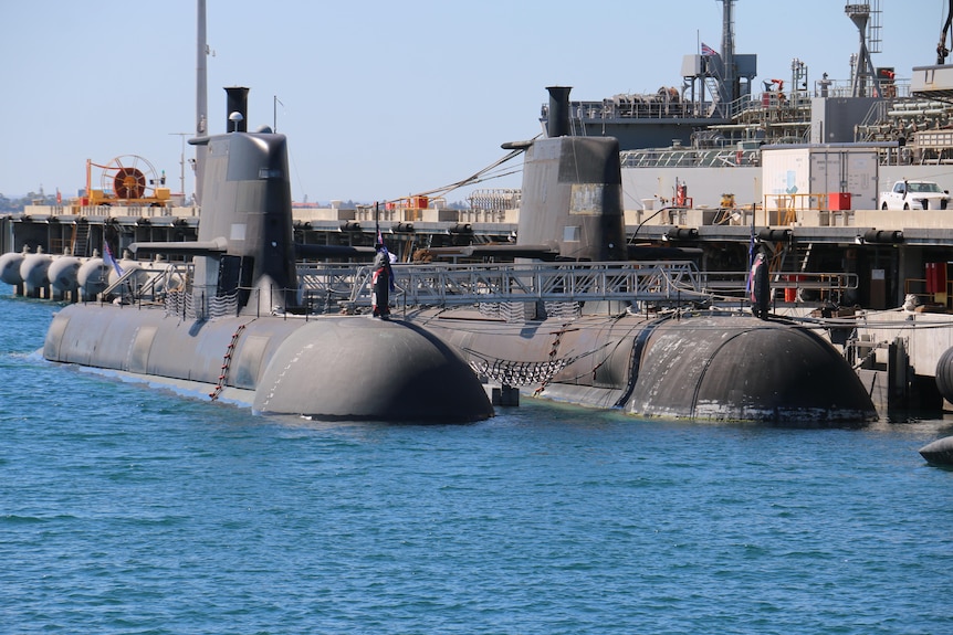 Submarines sit half submerged at a dock in the ocean