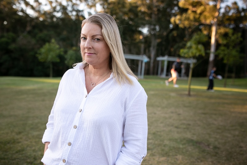 A woman wearing a white shirt stands in a peaceful park setting.