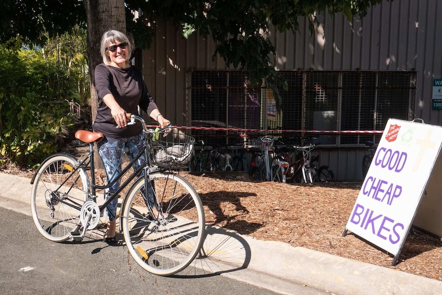 A woman stands behind her black bicycle.