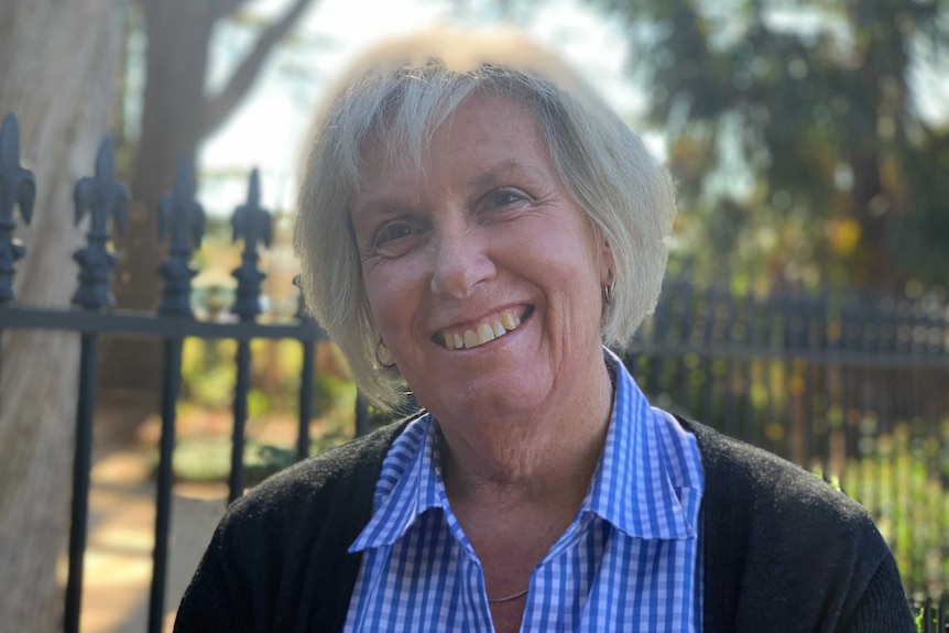 A smiling woman with blond hair wearing a cardigan and blue top standing outside.