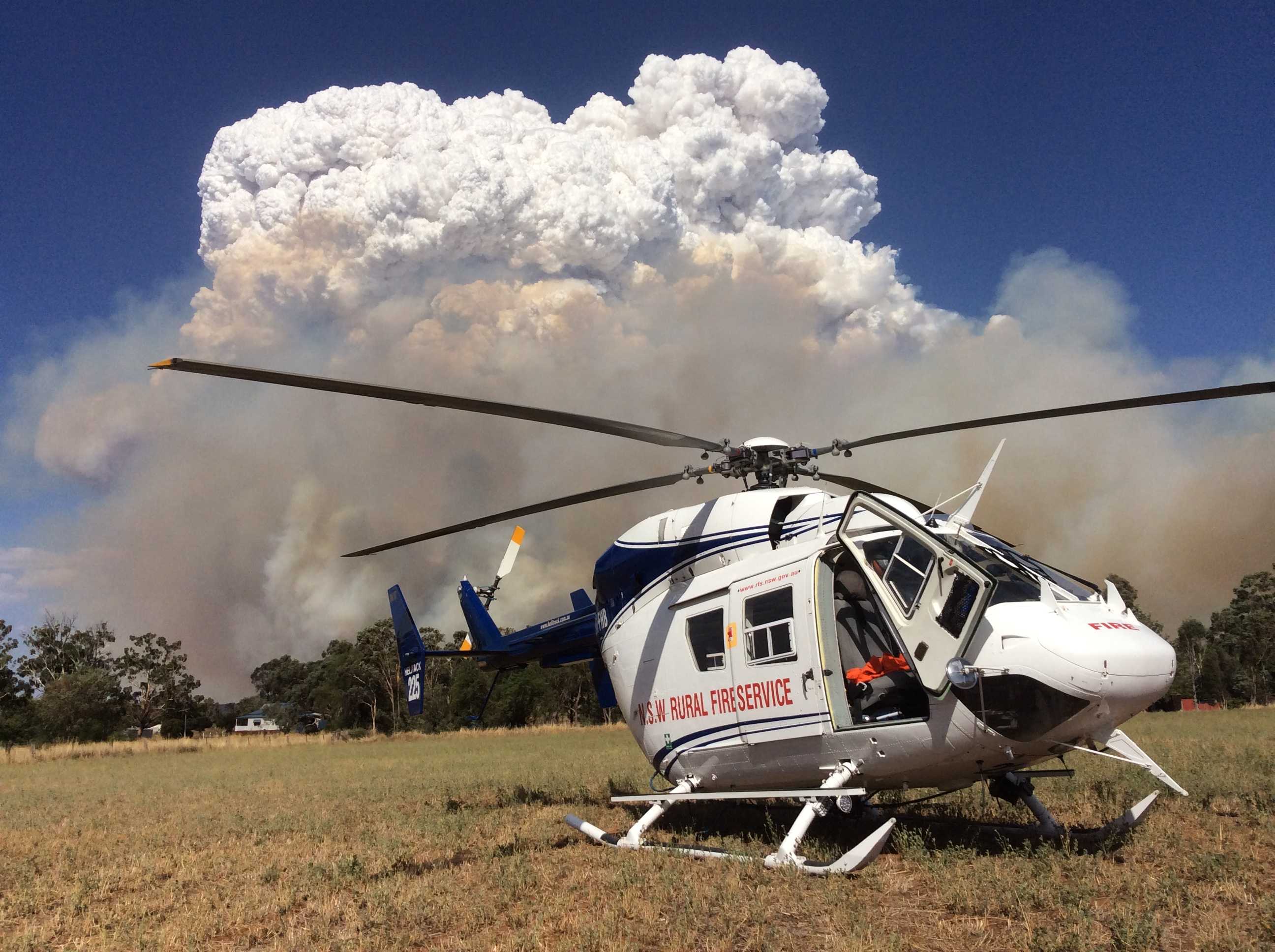 A stationary RFS helicopter in front of a large plume of smoke and cloud.