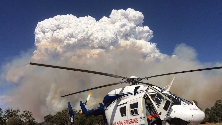 A stationary RFS helicopter in front of a large plume of smoke and cloud.