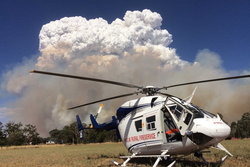 A stationary RFS helicopter in front of a large plume of smoke and cloud.
