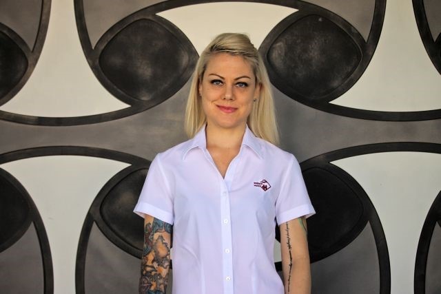 A young blonde woman in a white shirt in front of a painted background.