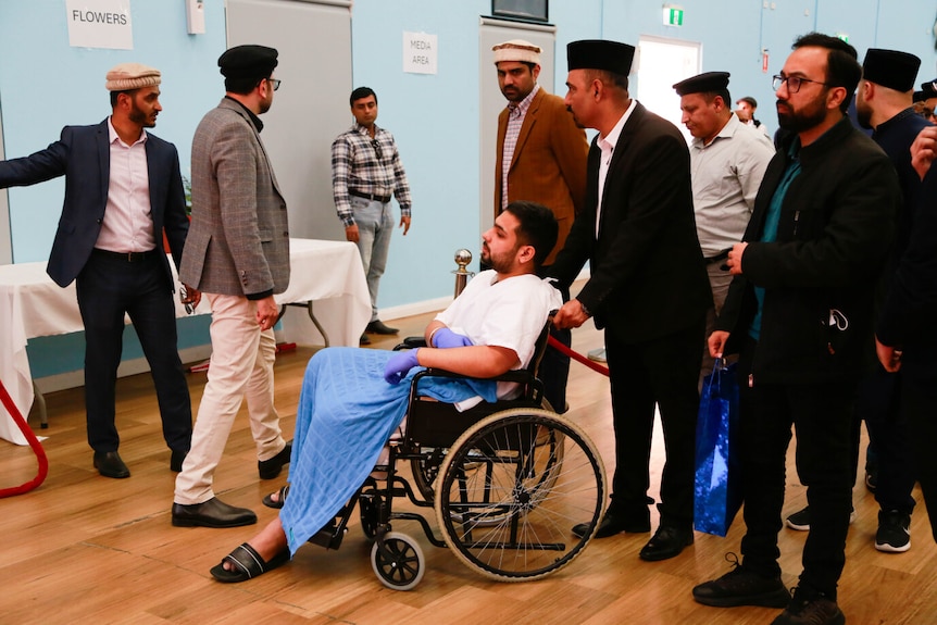 A man in a wheelchair is pushed across a floor surrounded by people.