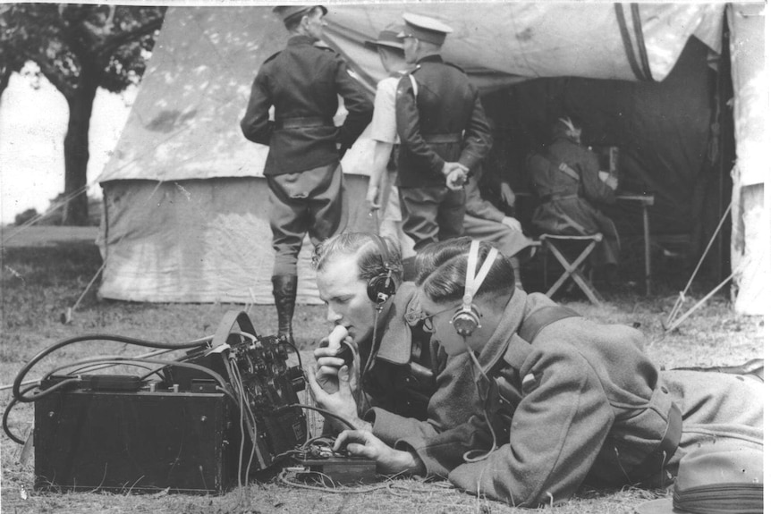 Black-and-white photo of two men in uniform crouched over a radio.