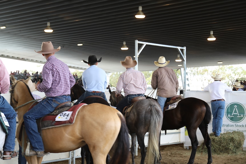 four men sit on horses next to an arena