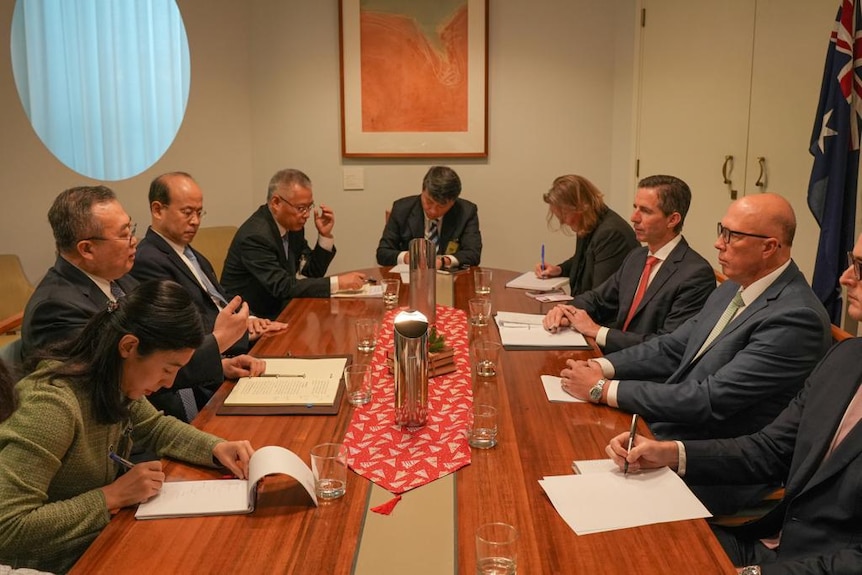 A group of officials sit around a wooden table, including Peter Dutton.