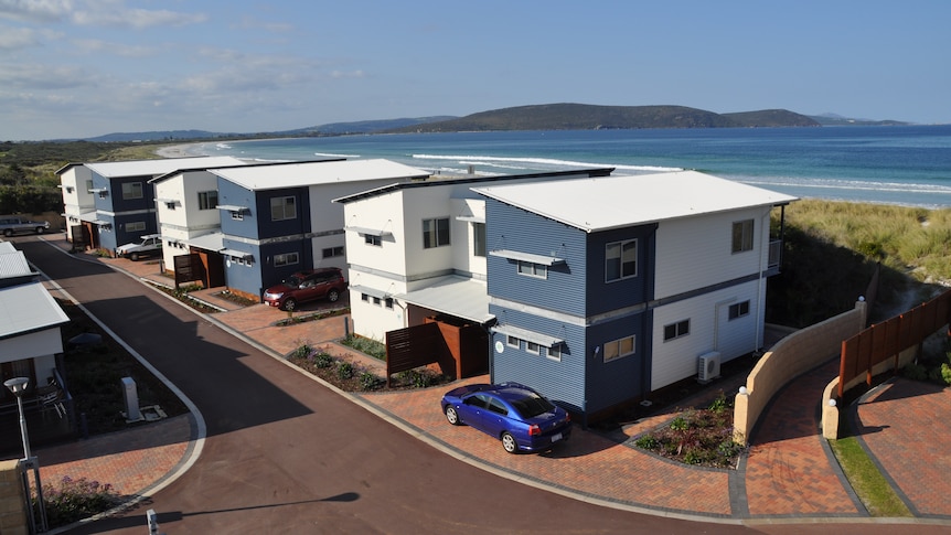 A row of whtei and blue houses next to the sea and distant mountains in the background.