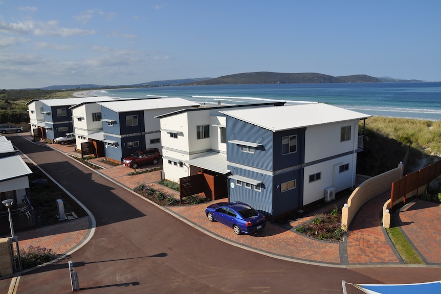 A row of whtei and blue houses next to the sea and distant mountains in the background.