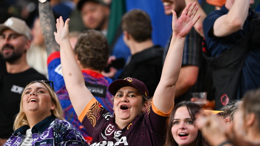 A Brisbane Broncos fan cheers and puts both hands in the air.